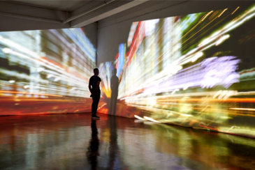 Man looking into a nighttime cityscape being projected in gallery space